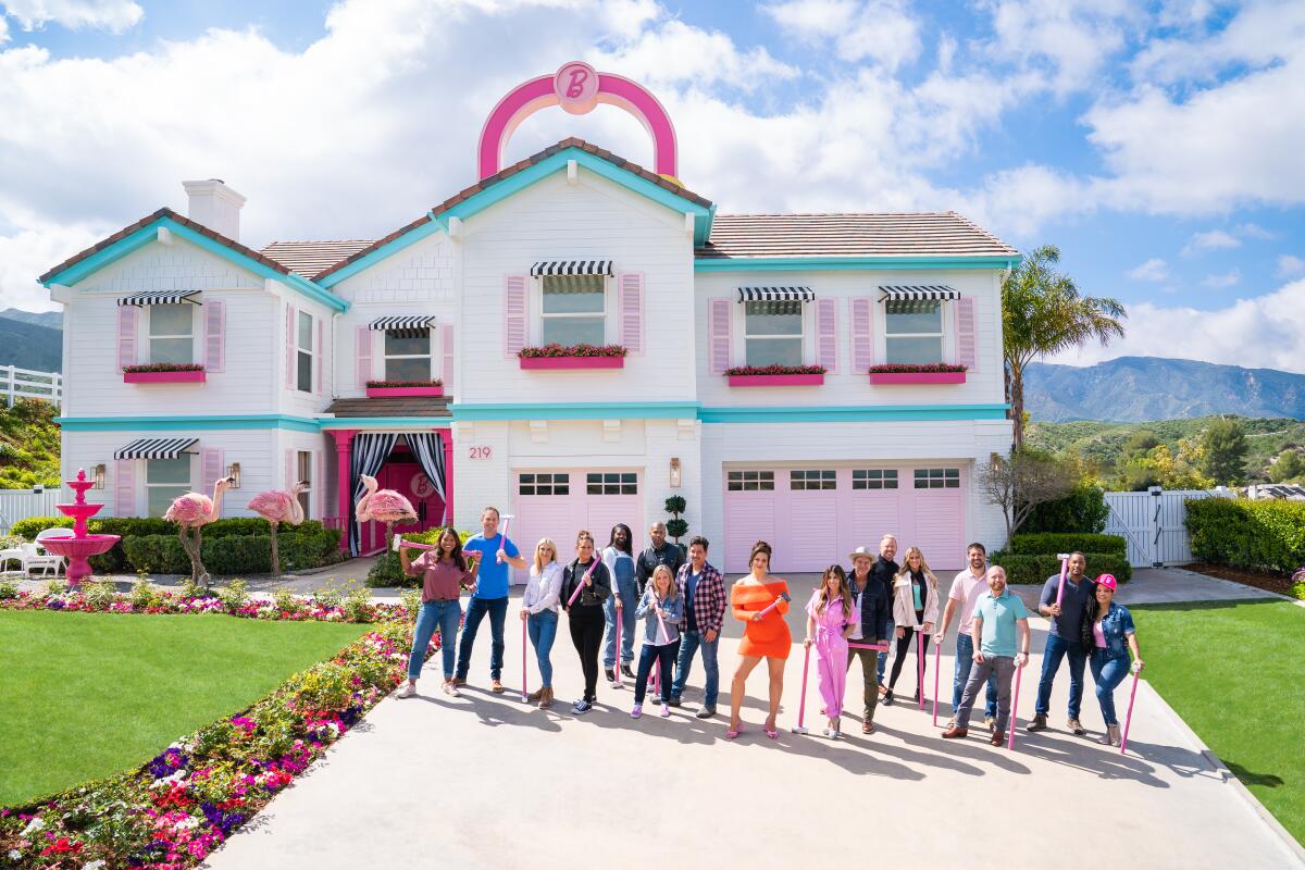 A line of people stand in front of a pink and teal house