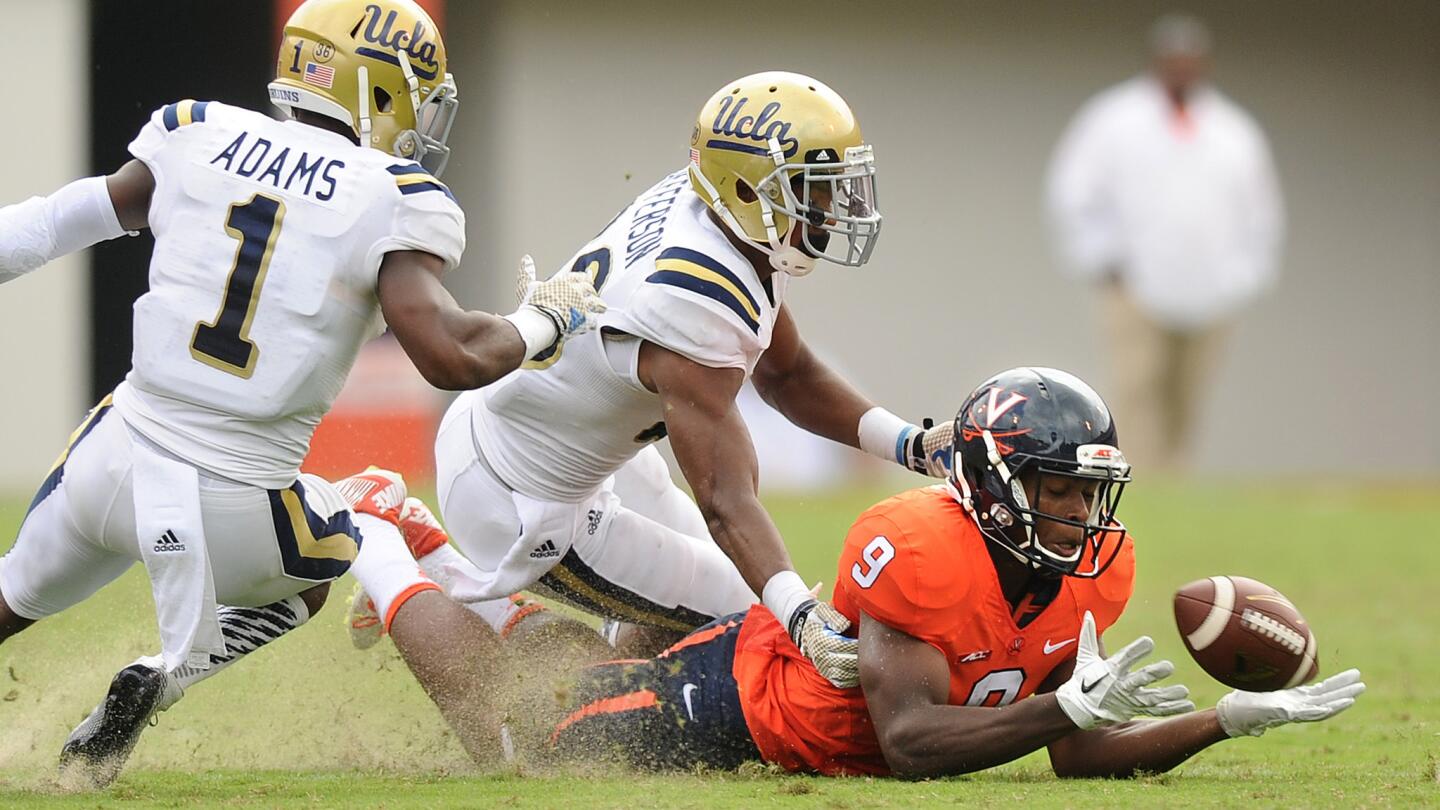 Virginia's Canaan Severin, right, can't make a catch in front of UCLA's Ishmael Adams, left, and Anthony Jefferson during the Bruins' 28-20 win Saturday.