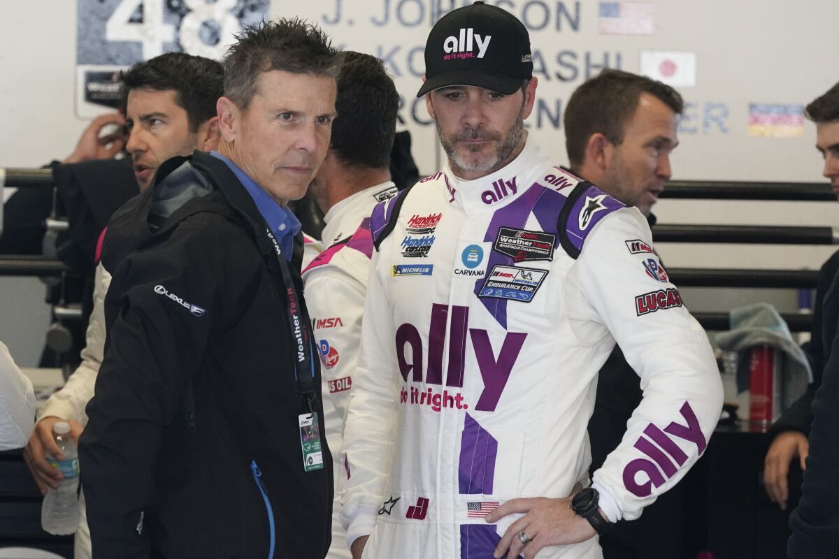 Retired driver Scott Pruett, left, and Jimmie Johnson talk in the Ally Cadillac Racing garage during practice for the Rolex 24 hour auto race at Daytona International Speedway, Thursday, Jan. 27, 2022, in Daytona Beach, Fla. (AP Photo/John Raoux)