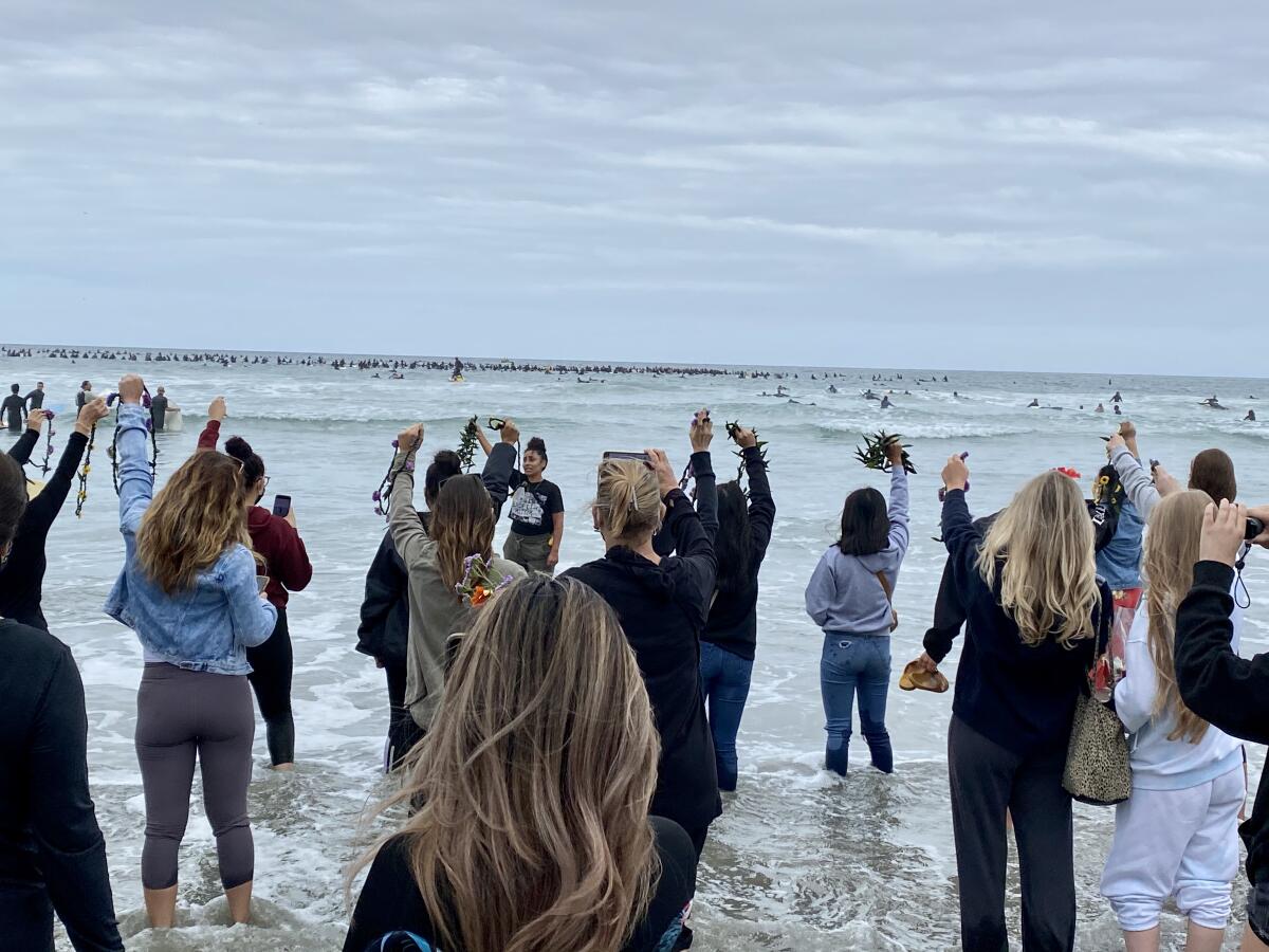 As surfers drop flowers in the waves, other protesters remain on the beach to do the same during the Paddle for Peace.