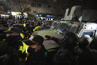 Police officers surround a military vehicle on a crowded street.