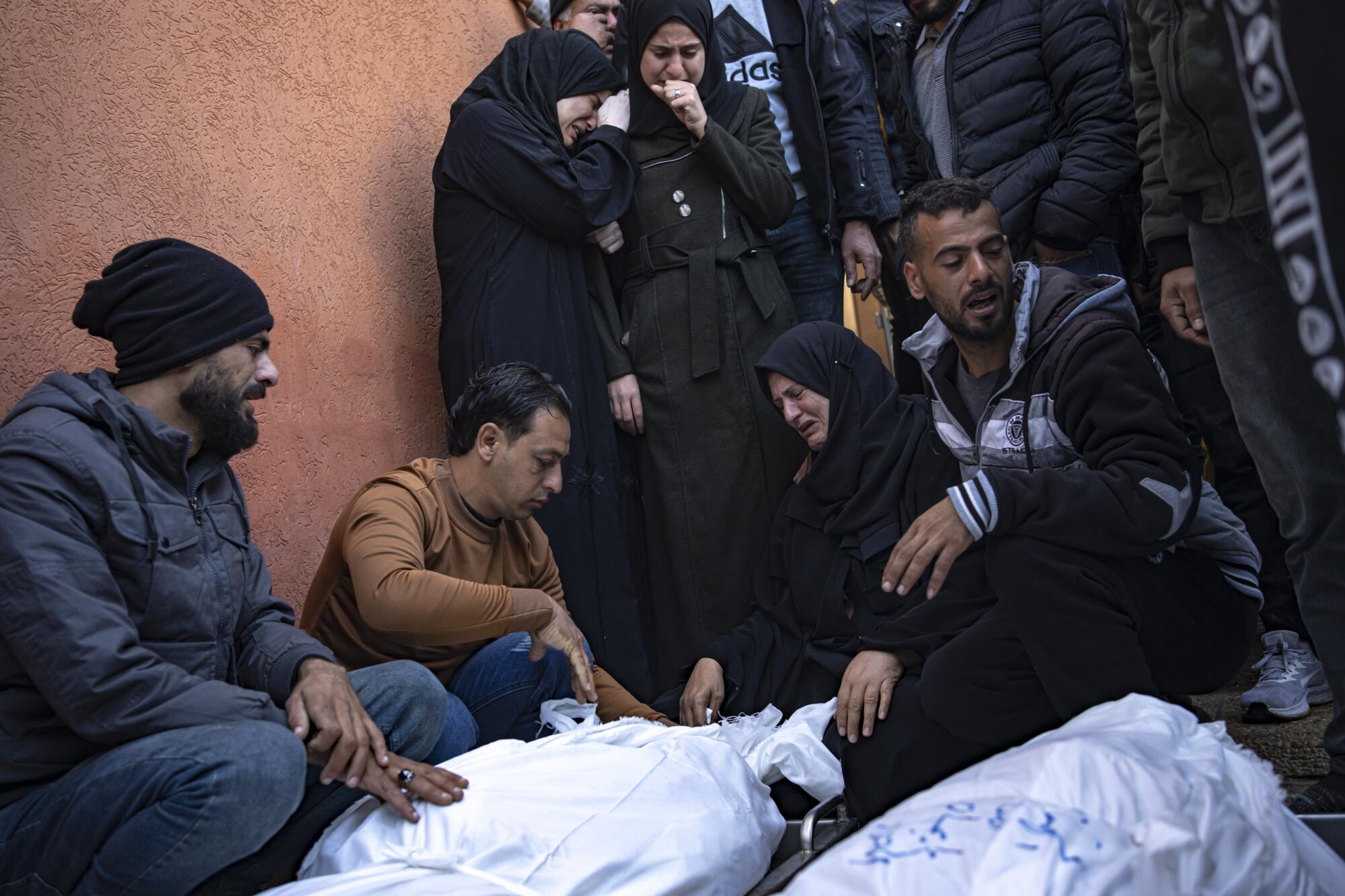 Palestinian men and women mourn near bodies wrapped in white. 