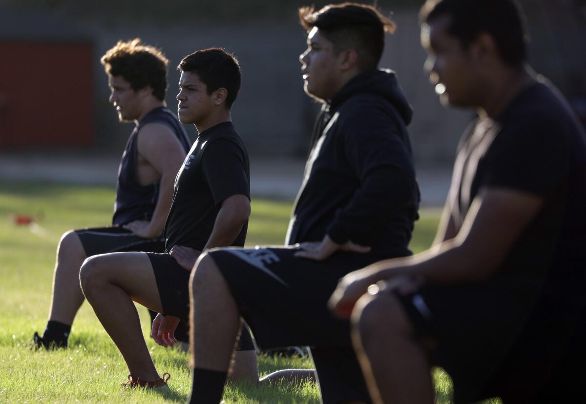 Taft High football players, spaced several feet apart, kneel as they exercise.