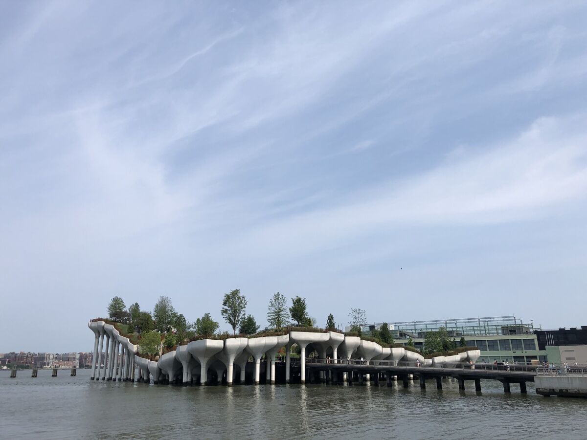 A broad view shows the tulip-like concrete forms of Little Island Park emerging from the Hudson River under a blue sky.