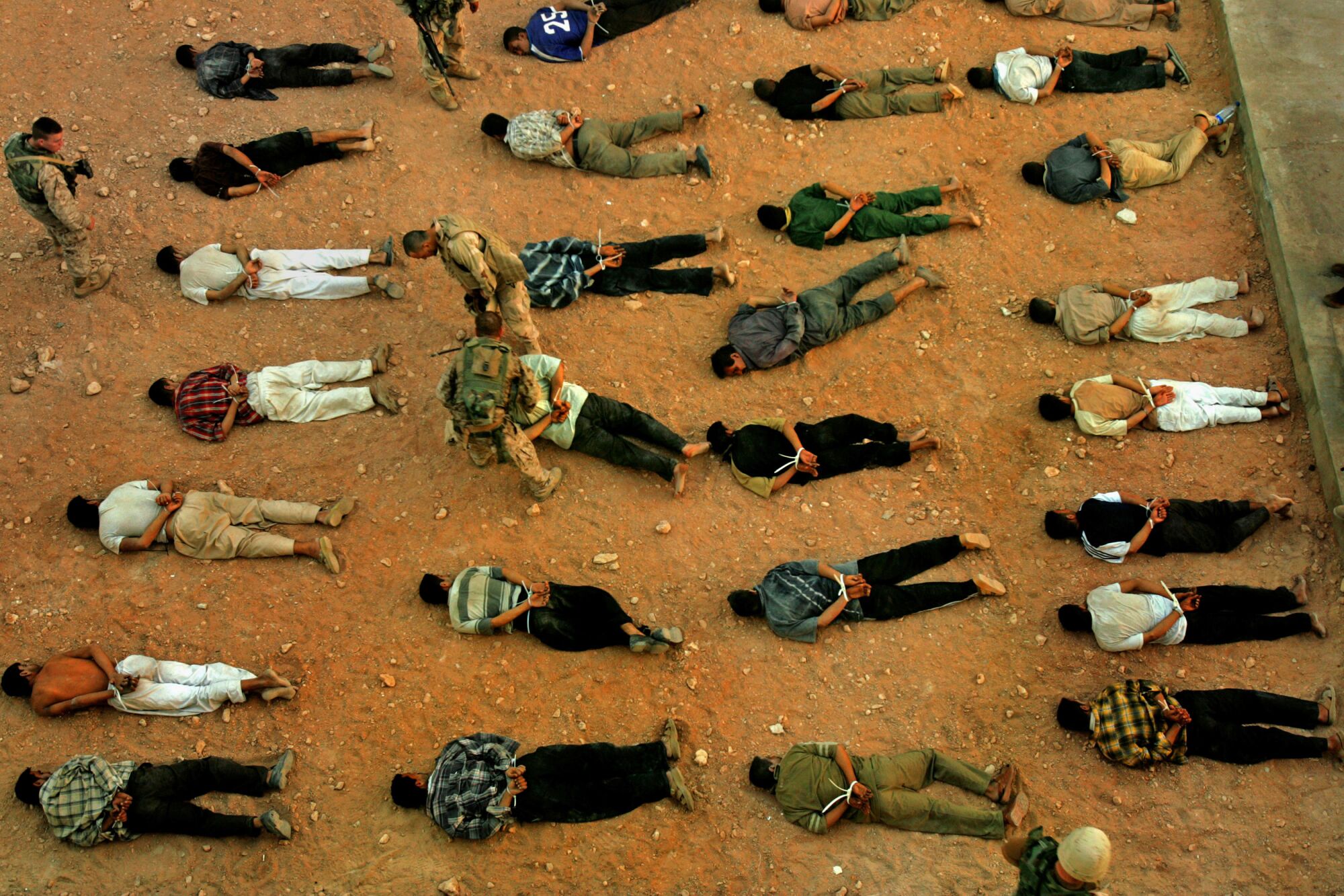 Rows of men lying face down in the dirt with their hands tied behind their backs