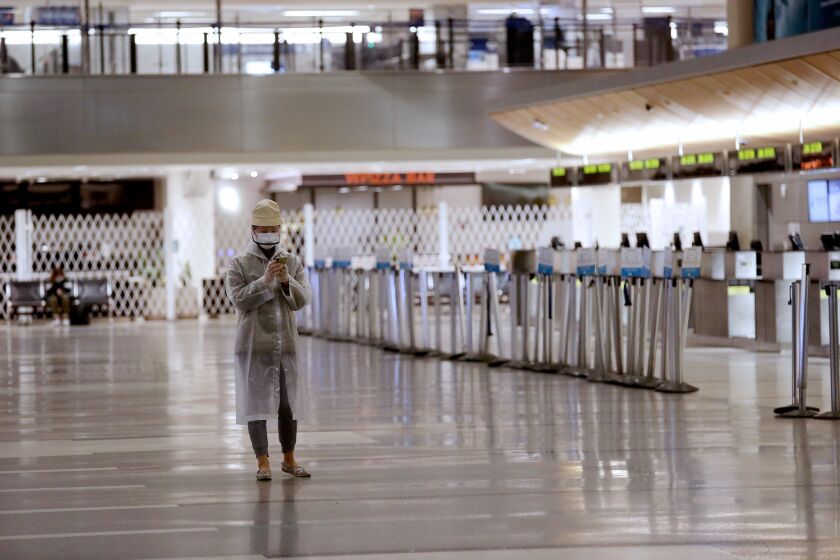 LOS ANGELES, CA -- APRIL 21: A lone passenger wearing personal protective equipment wonders through an empty Tom Bradley International Terminal as the coronavirus outbreak has brought passenger traffic to a near halt with travel down 95% at LosAngeles International Airport, the nation's second busiest, on Tuesday, April 21, 2020, in Los Angeles, CA. (Gary Coronado / Los Angeles Times)
