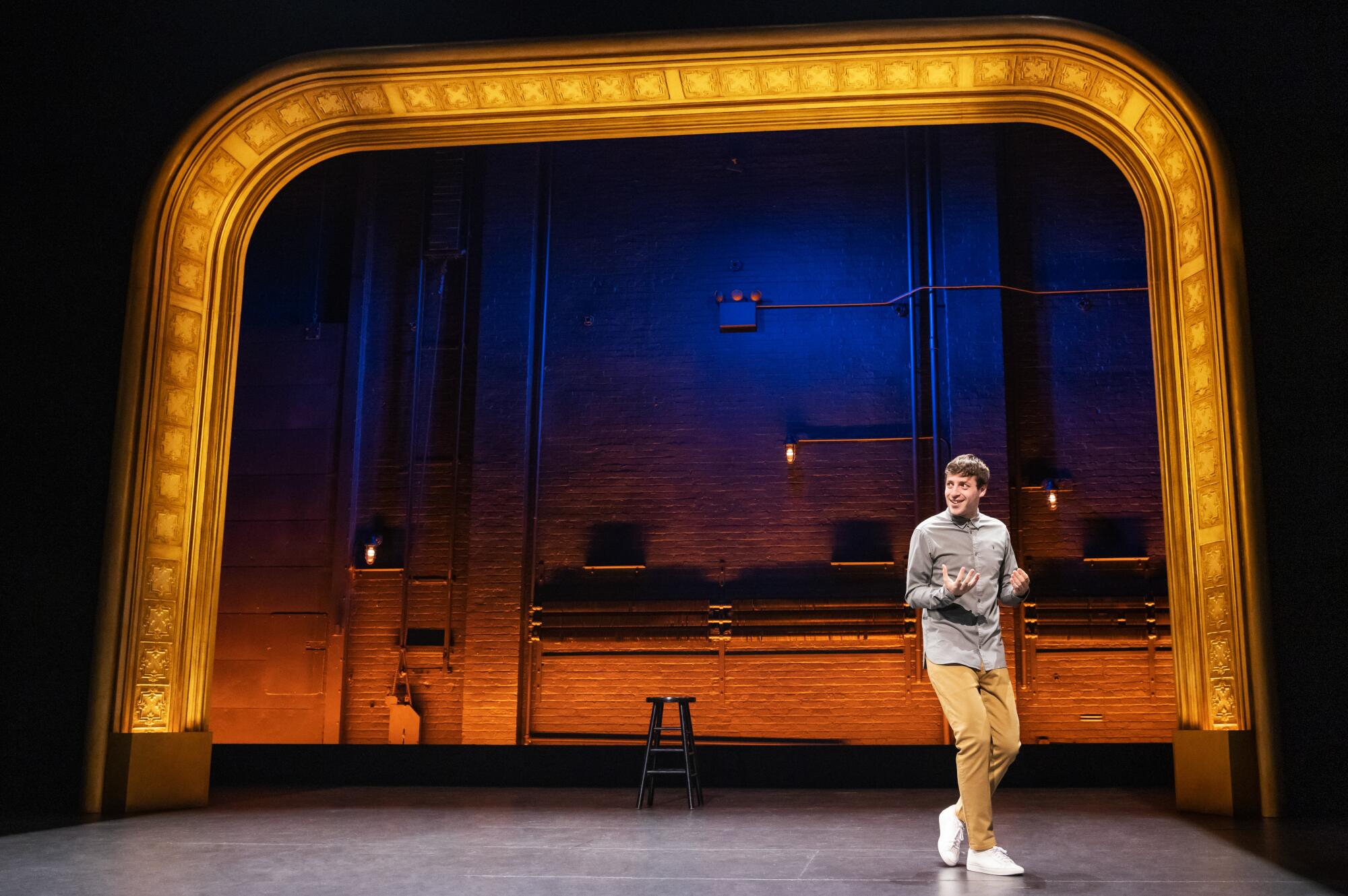 A casually dressed man onstage under a lighted arch