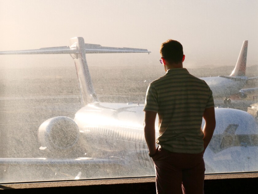 A man in an airport looks out at a plane under the setting sun
