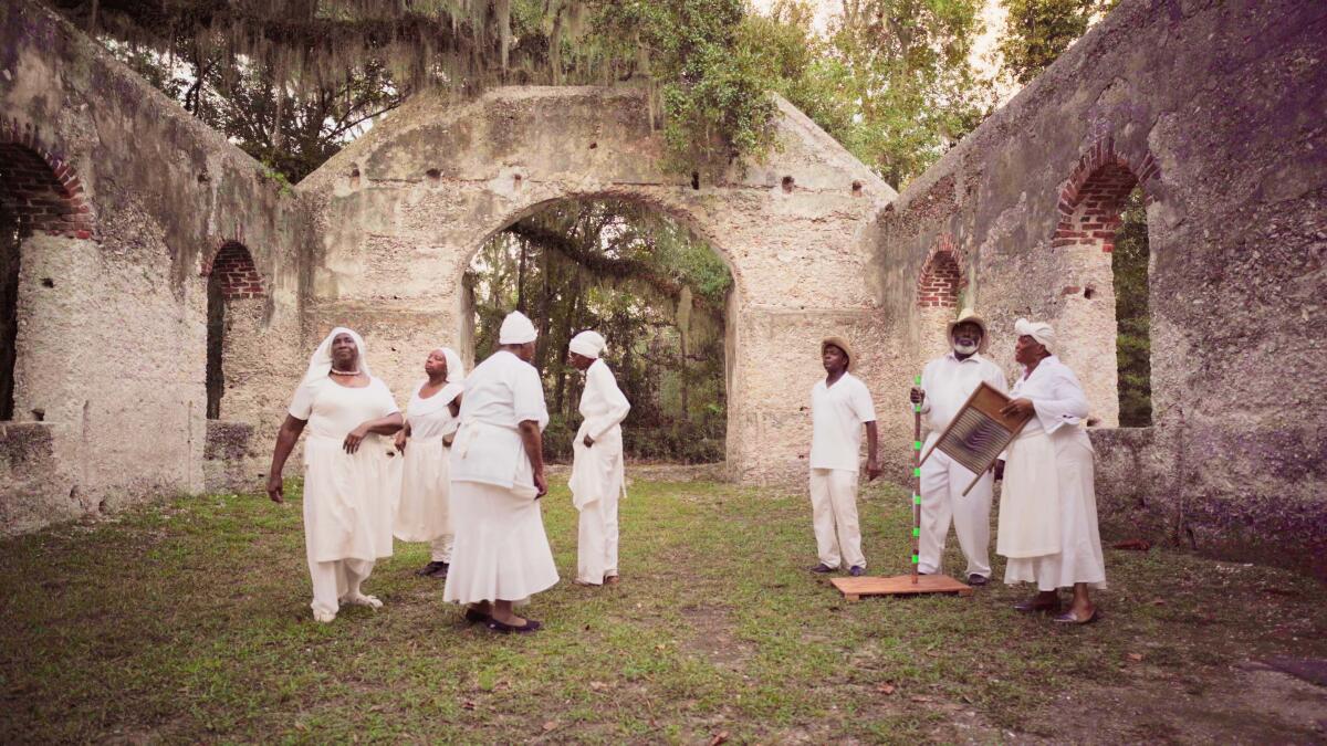 Several people stand on grass in the daylight surrounded by the walls of an old structure