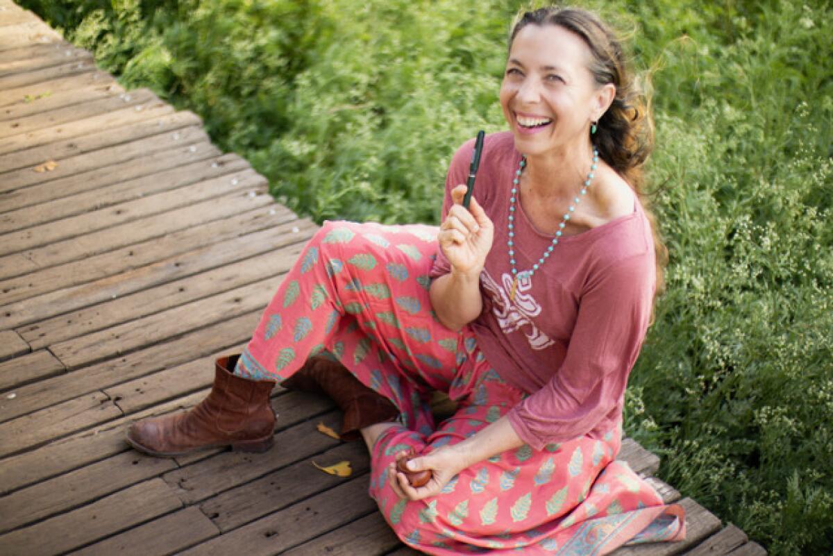 A woman seated on a wooden deck holds a pen.