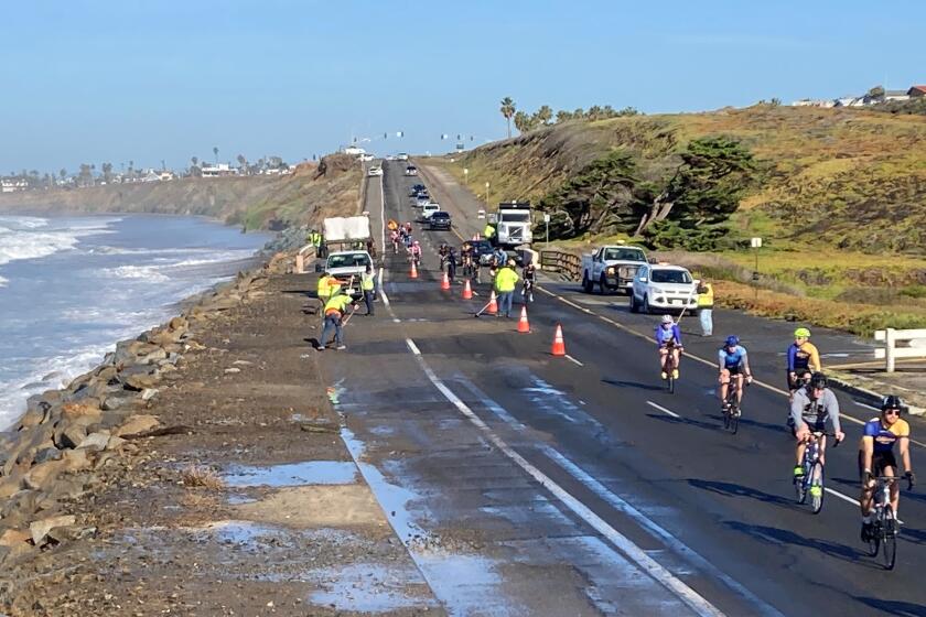 Cyclists pass a road-cleaning crew on Carlsbad Boulevard after a high tide in January.