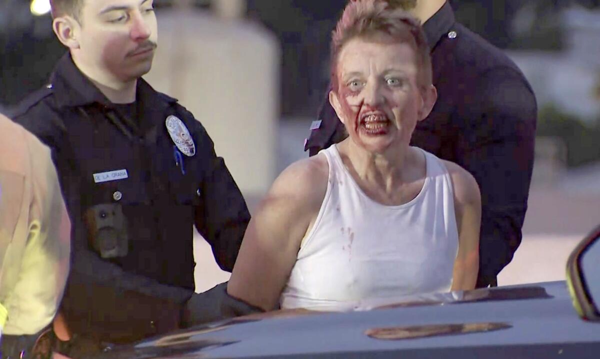 Police arrest a woman wearing a white tank top who whose face and mouth are bloodied.