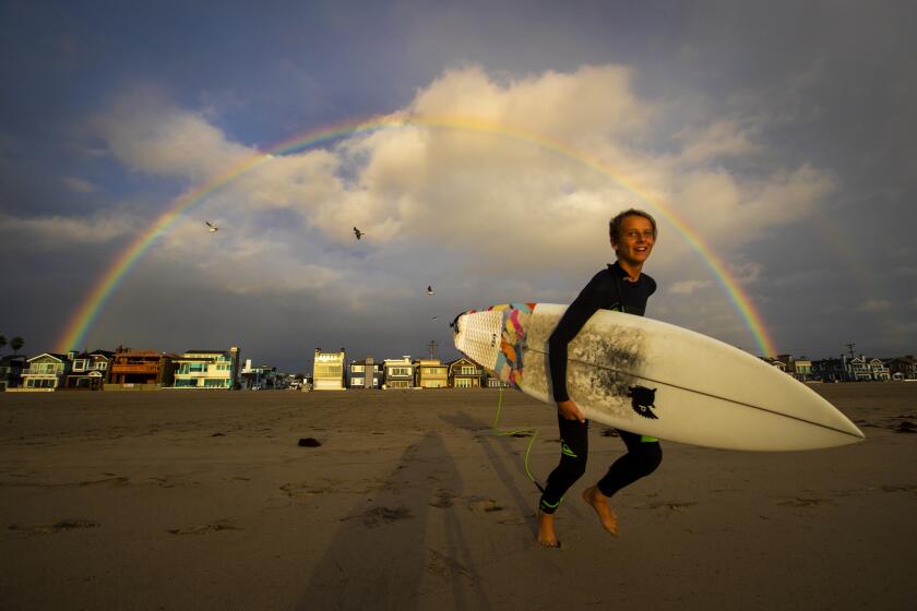 NEWPORT BEACH, CALIF. -- WEDNESDAY, MARCH 13, 2019: Surfer Jonah Haack, 13, of Newport Beach, revels in the appearance of a rainbow and excellent overhead surf conditions in between rain showers in Newport Beach, Calif., on March 13, 2019. (Allen J. Schaben / Los Angeles Times)