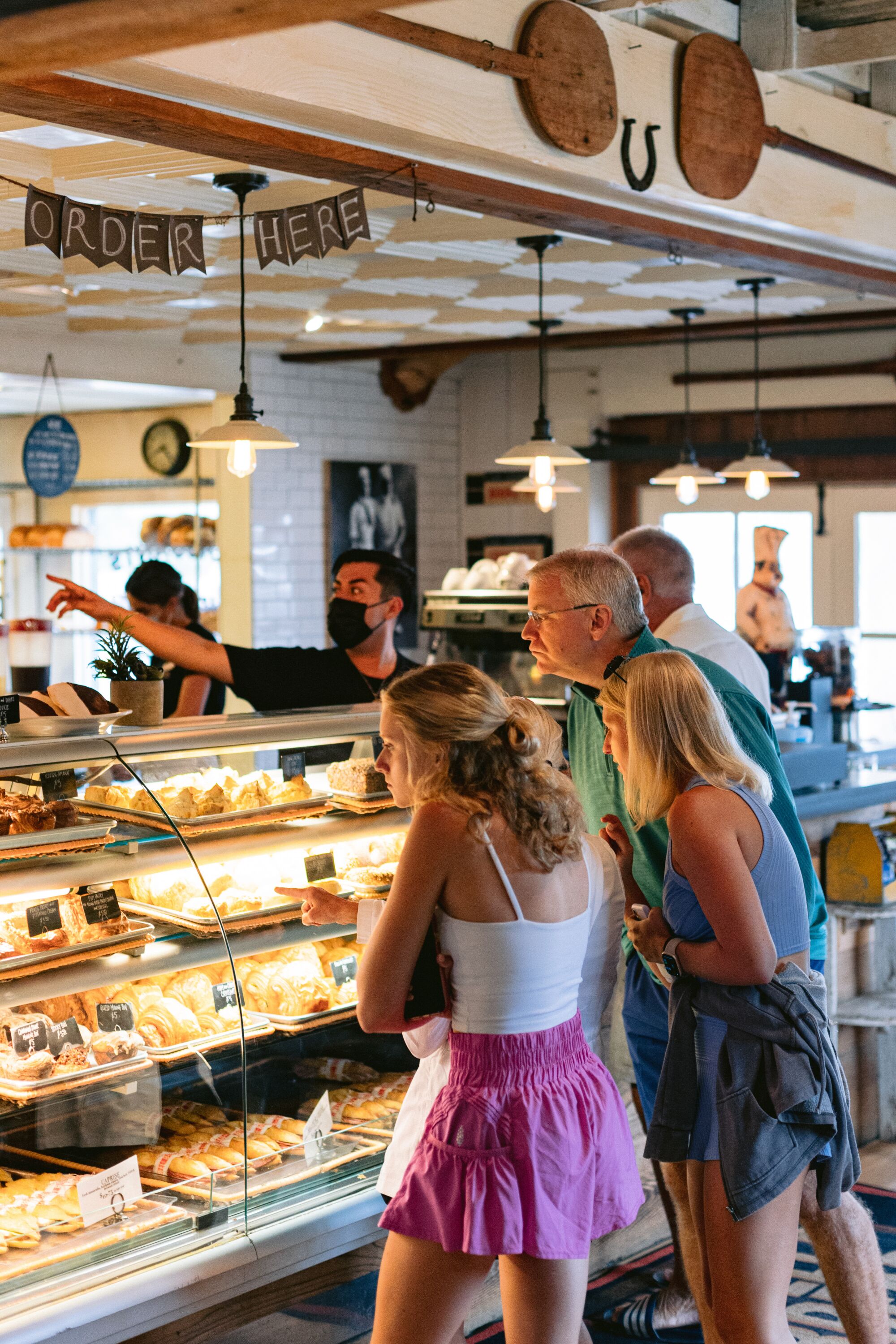 People standing in front of a bakery display, craning necks to see what's inside, in a bakery.