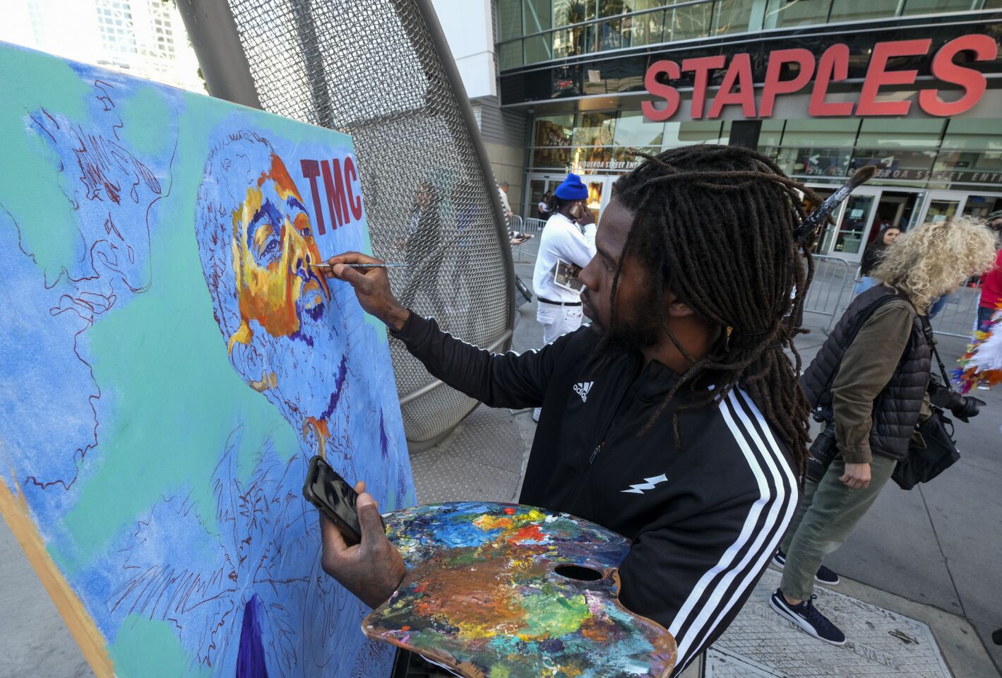 Artist Gift Davis works on a portrait of rapper Nipsey Hussle as fans wait in line to attend a public memorial at Staples Center.