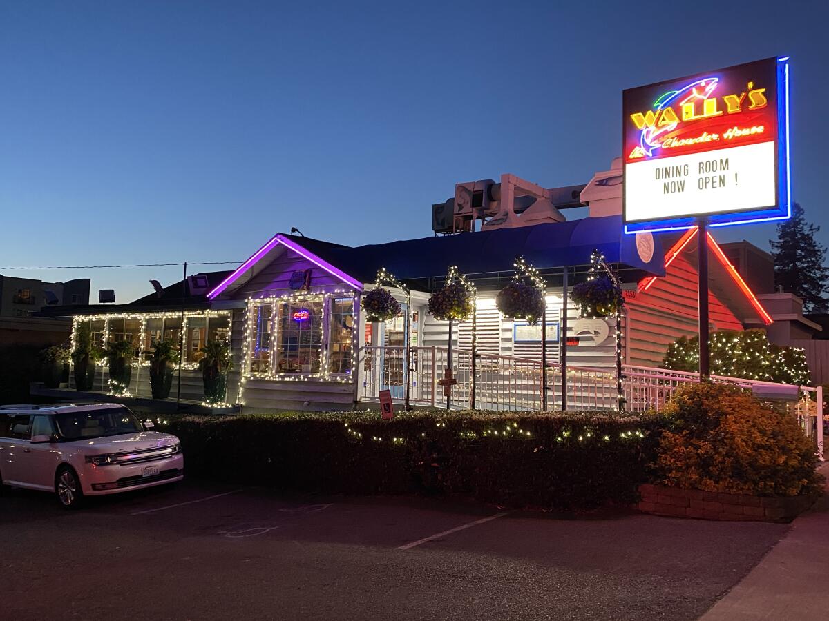 A restaurant decorated in lights advertises on a signboard that its dining room is open.