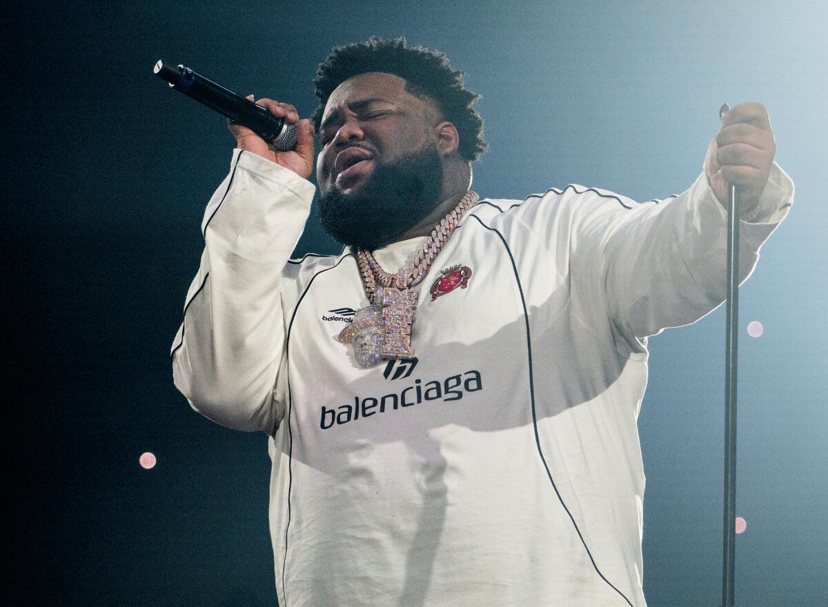 Rod Wave raps into a hand-held microphone while holding the mic stand with his other hand onstage