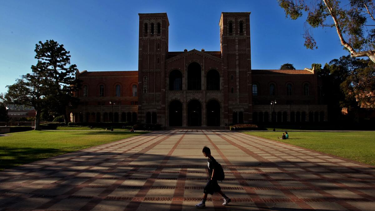 Royce Hall and its two towers loom in the background as a student walks on the UCLA campus.