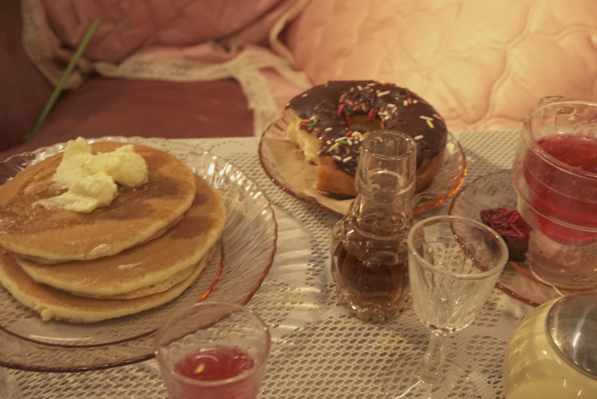 A closeup of pancakes, a chocolate doughnut and glassware on a table.
