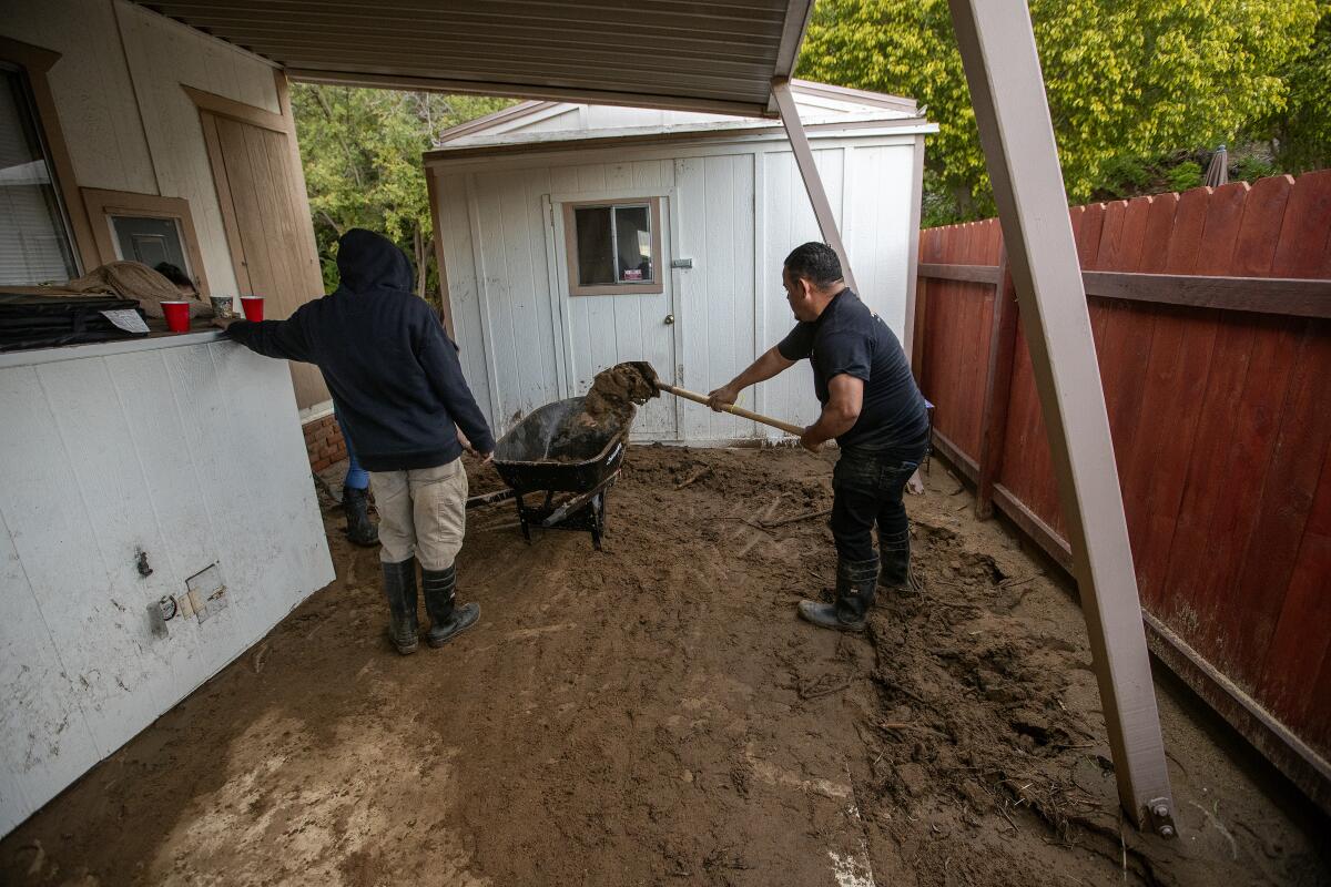 Workers clear mud from the driveway of the modular home the Rivas family rents in West Hills, which was damaged by a mudslide.