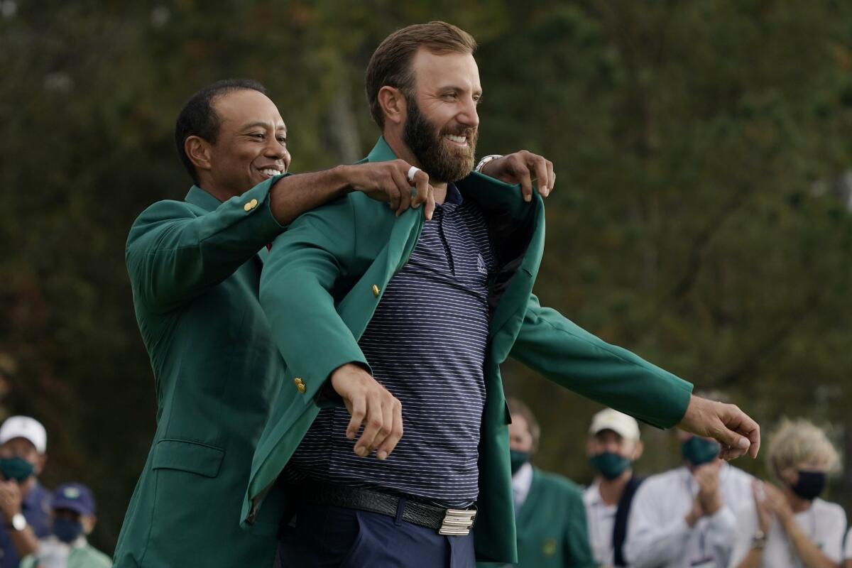 Tiger Woods helps Masters’ champion Dustin Johnson with his green jacket after his victory at the Masters.