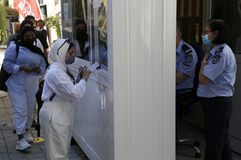 A woman wearing protective face mask, shows her COVID-19 test to a police officer at Ledra crossing point in divided capital Nicosia, Cyprus, Friday, June 4, 2021. Ethnically split Cyprus took a key step toward a return to its normal rhythms of life amid the pandemic on Friday when nine crossing points along a United Nations-controlled buffer zone were reopened, enabling ordinary Cypriots to cross the divide. (AP Photo/Petros Karadjias)