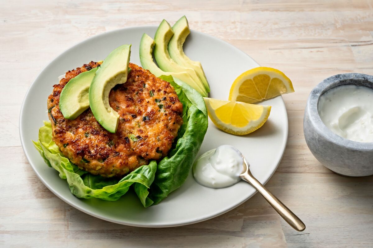 A salmon patty is placed on a bed of lettuce and topped with slices of avocado.