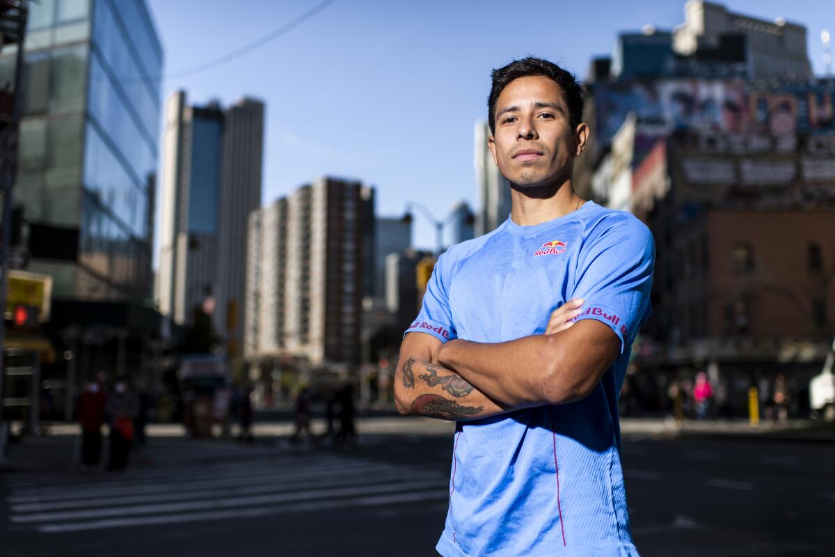 A young man stands in the street with his arms crossed in front of his chest