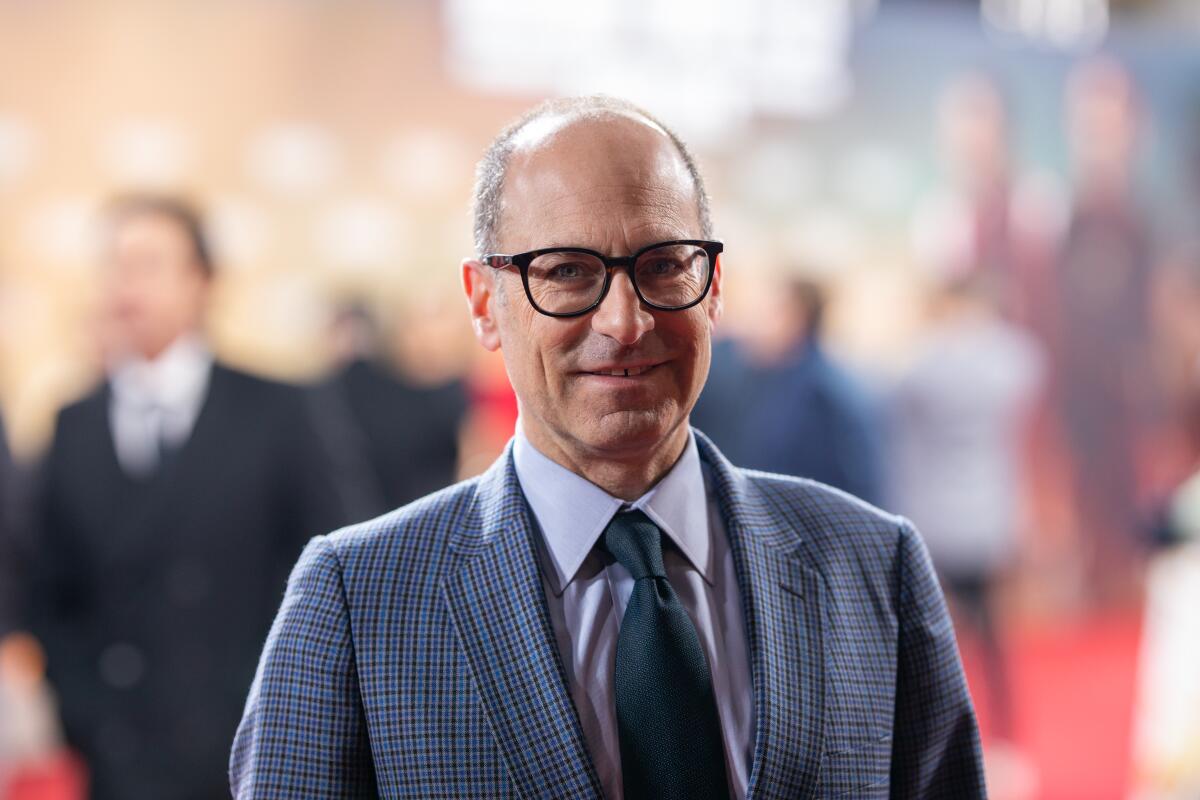 A smiling man in glasses and a suit at a film premiere.