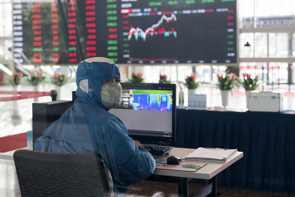 A worker wearing a protective suit reacts in front of an infrared temperature machine in the lobby of the Shanghai Stock Exchange building in Shanghai, China, Friday, Feb. 14, 2020. Asian shares mostly fell Friday as investors turned cautious following a surge in cases of a new virus in China that threatens to crimp economic growth and hurt businesses worldwide. (AP Photo)
