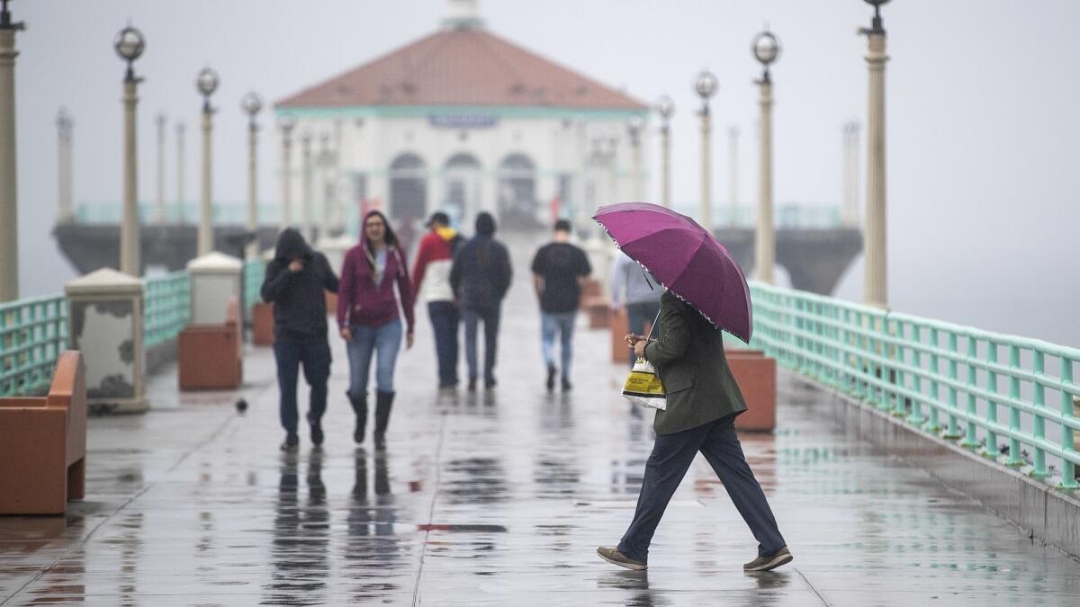 People use umbrellas and bundle up with rain jackets while walking down the pier amid light rain showers in Manhattan Beach on Feb. 28Thursday.