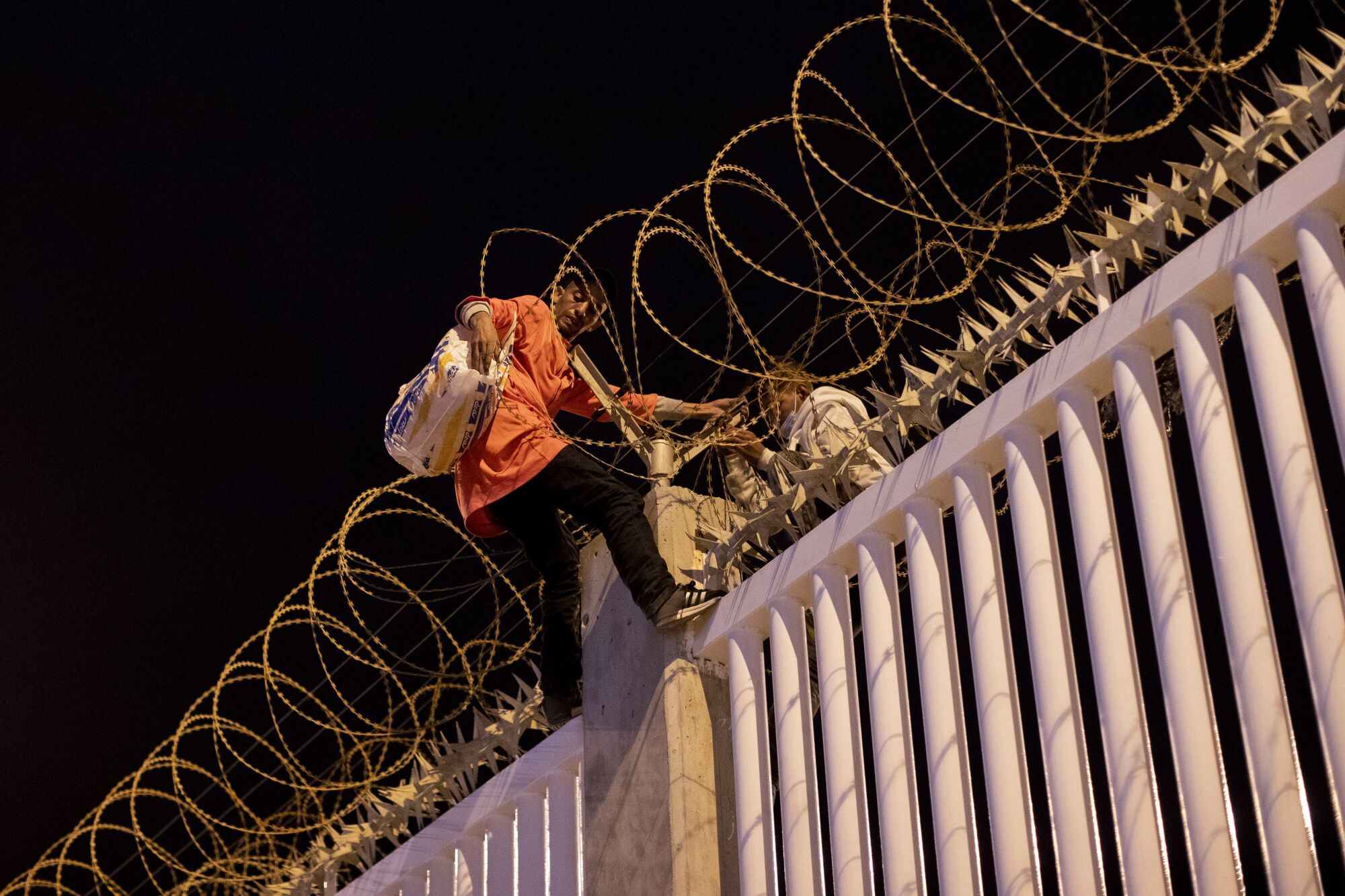 Two men climb over a razor-wire-topped fence in the night