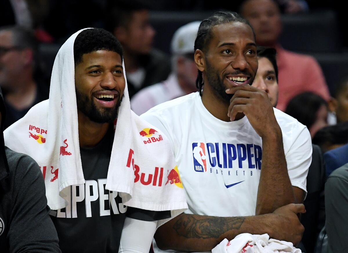 Clippers forwards Paul George, left, and Kawhi Leonard watch their teammates finish off a 120-99 victory over the Phoenix Suns on Dec. 17, 2019, at Staples Center.