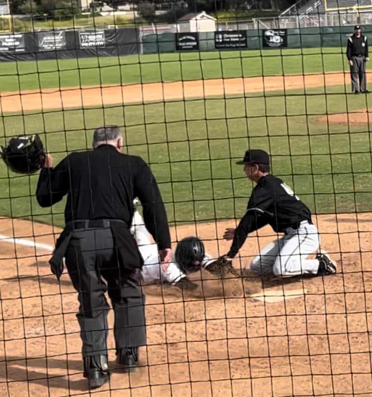 A pitcher tags out a runner at home plate in a baseball game as an umpire watches before making a call.