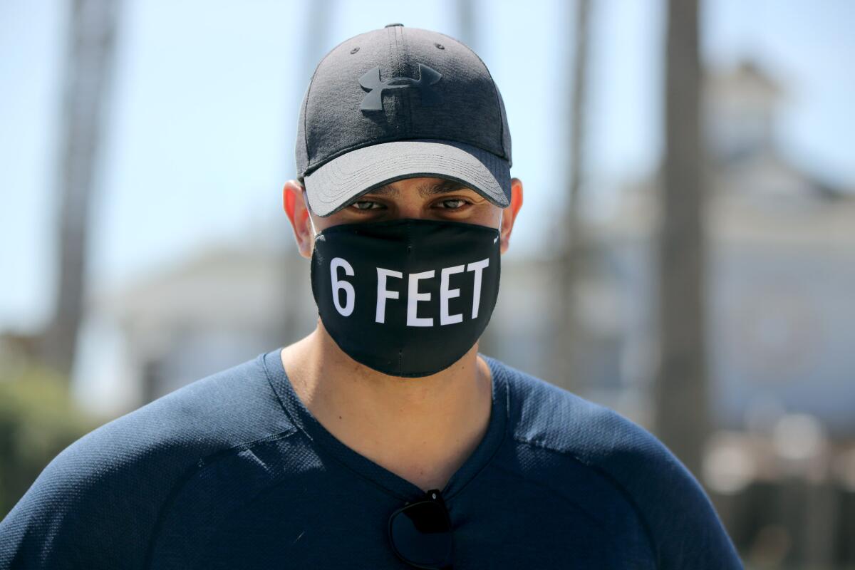 A man wears a black face mask that says "6 feet" on it. 
