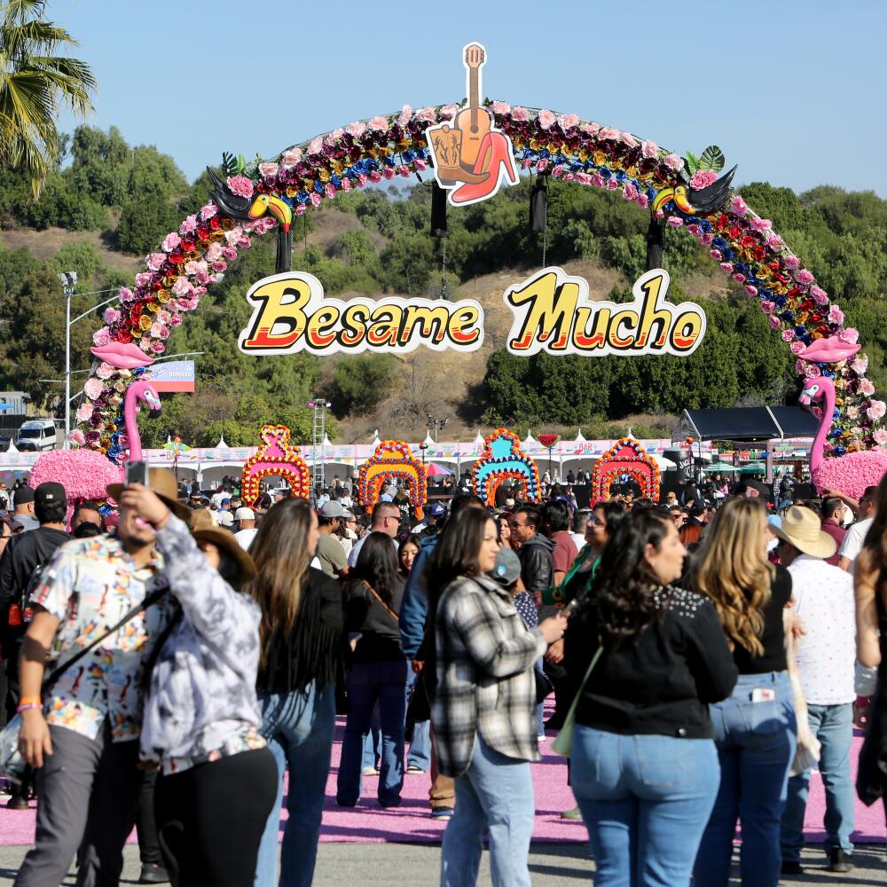 A large crowd stands in front of a Besame Mucho sign