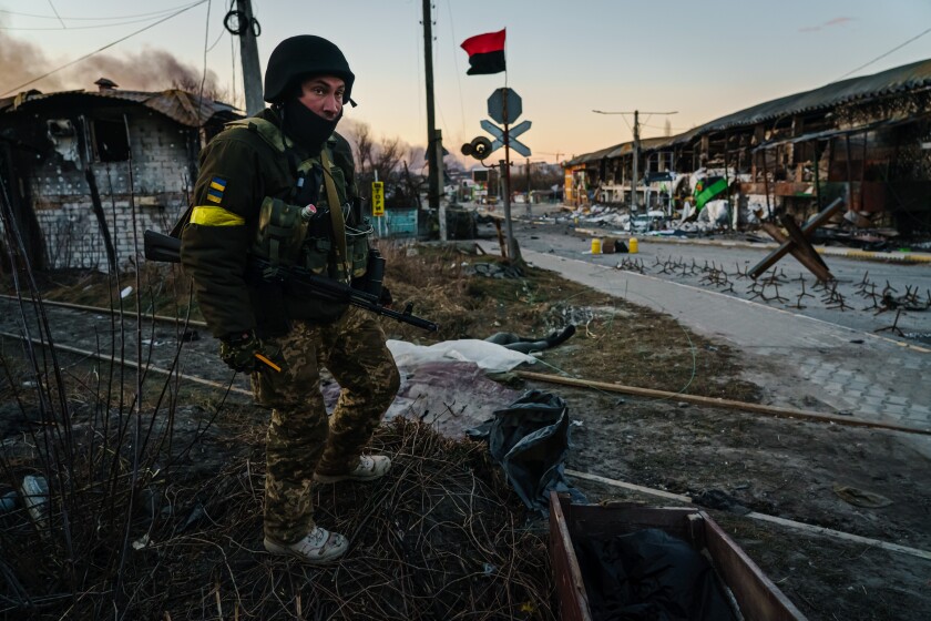 A soldier stands near covered bodies after fighting in Ukraine.