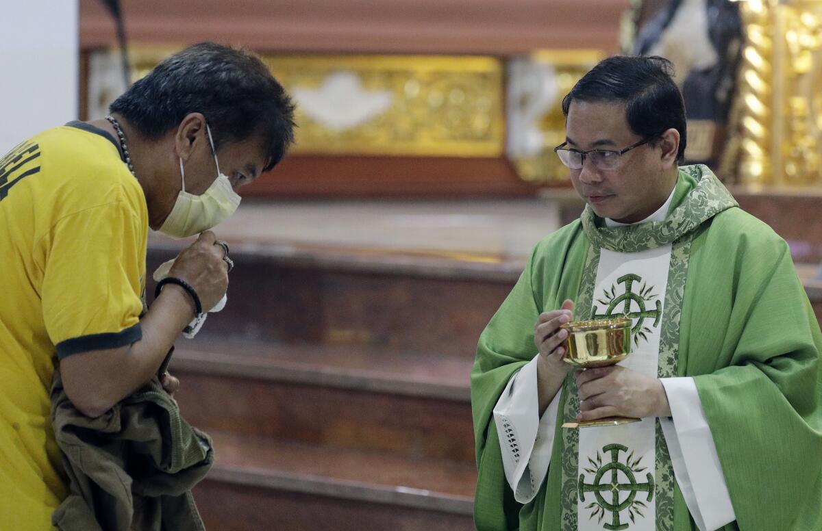 In this Feb. 10, 2020, photo, Catholic priest Fr. Joseph Arellano, right, looks at a man who forgot to take off his protective mask and tried to insert the host in his mouth during communion at a mass at the Minor Basilica of San Lorenzo Ruiz in Manila's Chinatown, Philippines.