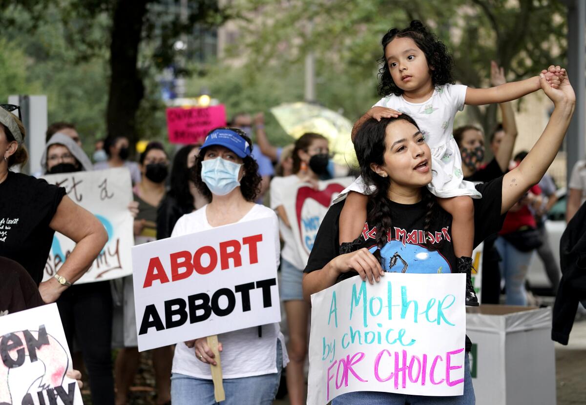 A woman holds her young daughter surrounded by other protesters, some carrying signs