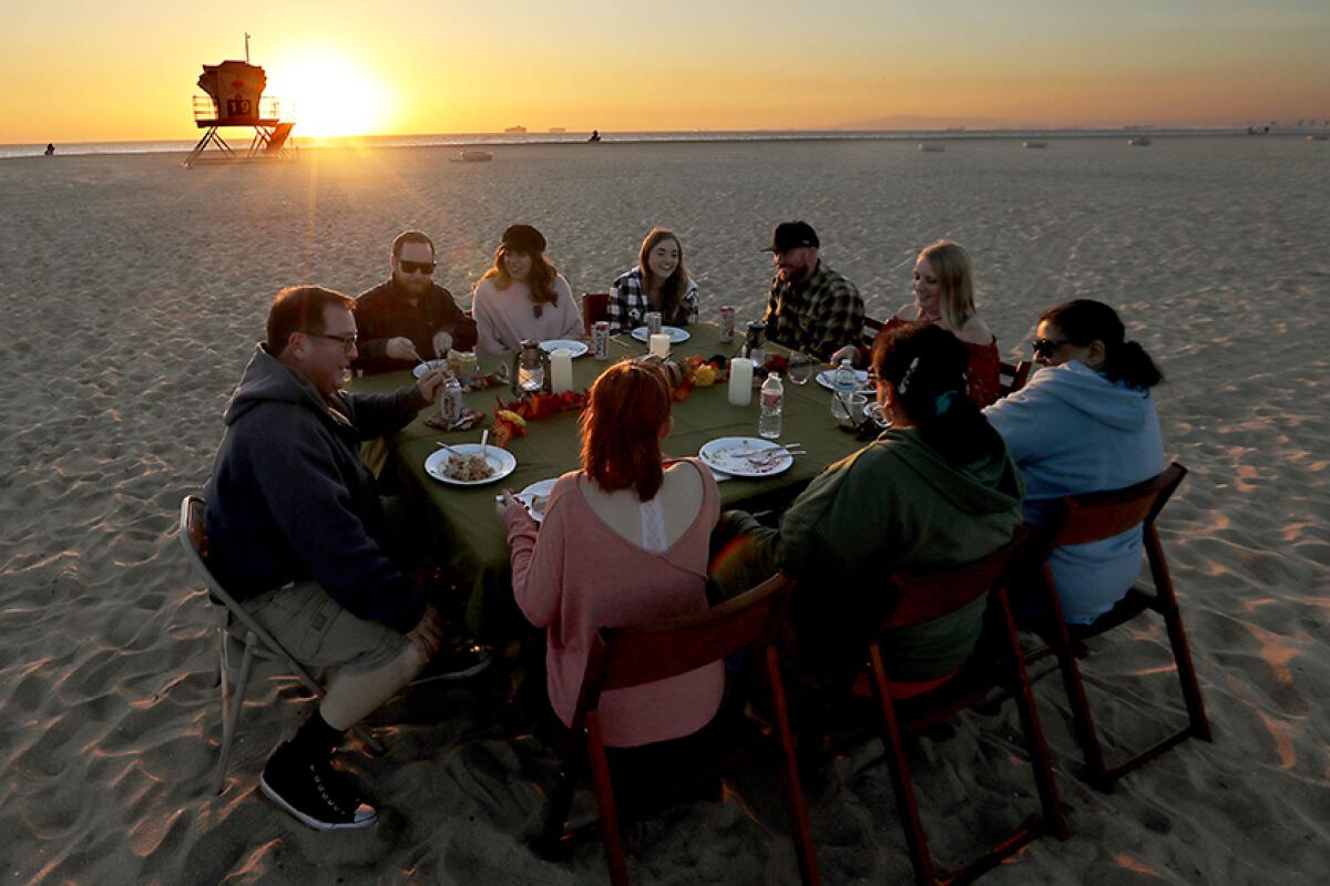 Members of a family celebrate an outdoor Thanksgiving dinner on the sand at a beach as the sun sets