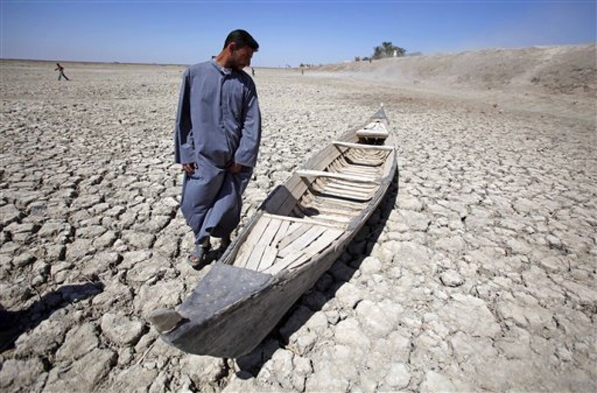 In this photo taken Friday, March 27, 2009, Akeed Abdullah stands next to his boat in a dried marsh in Hor al-Hammar in southern Iraq. A severe drought is threatening Iraq's southern marshes, the traditional site of the biblical Garden of Eden, just as the region was recovering from Saddam Hussein's draining of its lakes and swamps to punish a political rebellion. (AP Photo/Hadi Mizban)