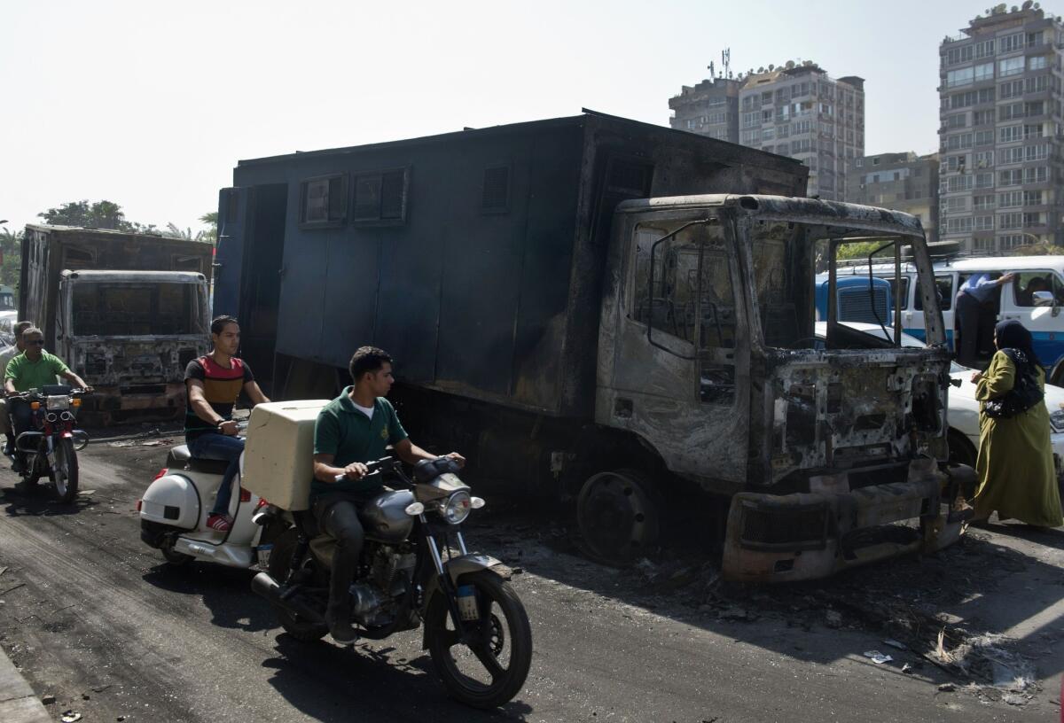 Motorcyclists pass by a burnt-out police vehicle on Monday in Cairo that was set on fire by government opponents the night before during clashes with riot police.