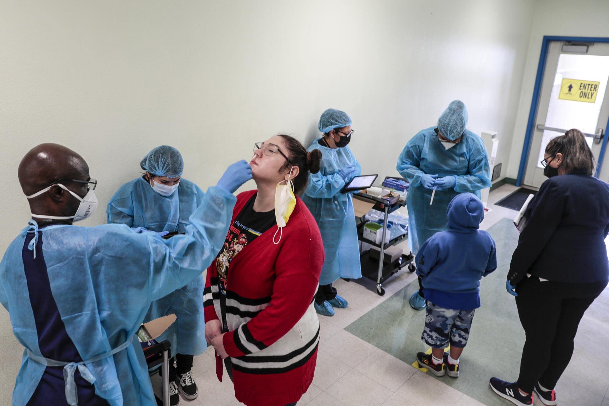 A woman surrounded by health workers in protective gear leans her head back for a nasal swab test.