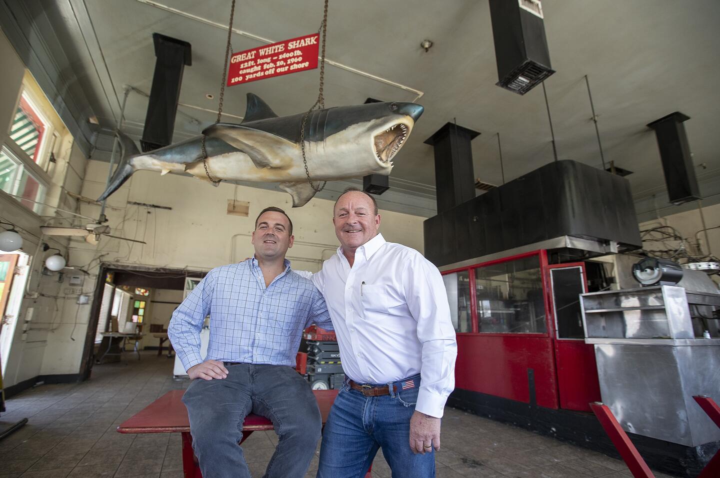 Jimmy Wasko and his father, Jim, pose under a preserved great white shark at the Crab Cooker, their Newport Beach restaurant that will be torn down and rebuilt. The shark was caught in Newport in 1960, according to the sign dangling above it.