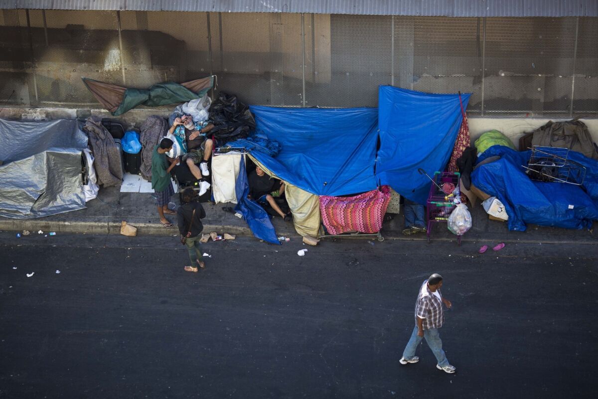 Tarps used for shelter fill a city sidewalk as people talk with one another