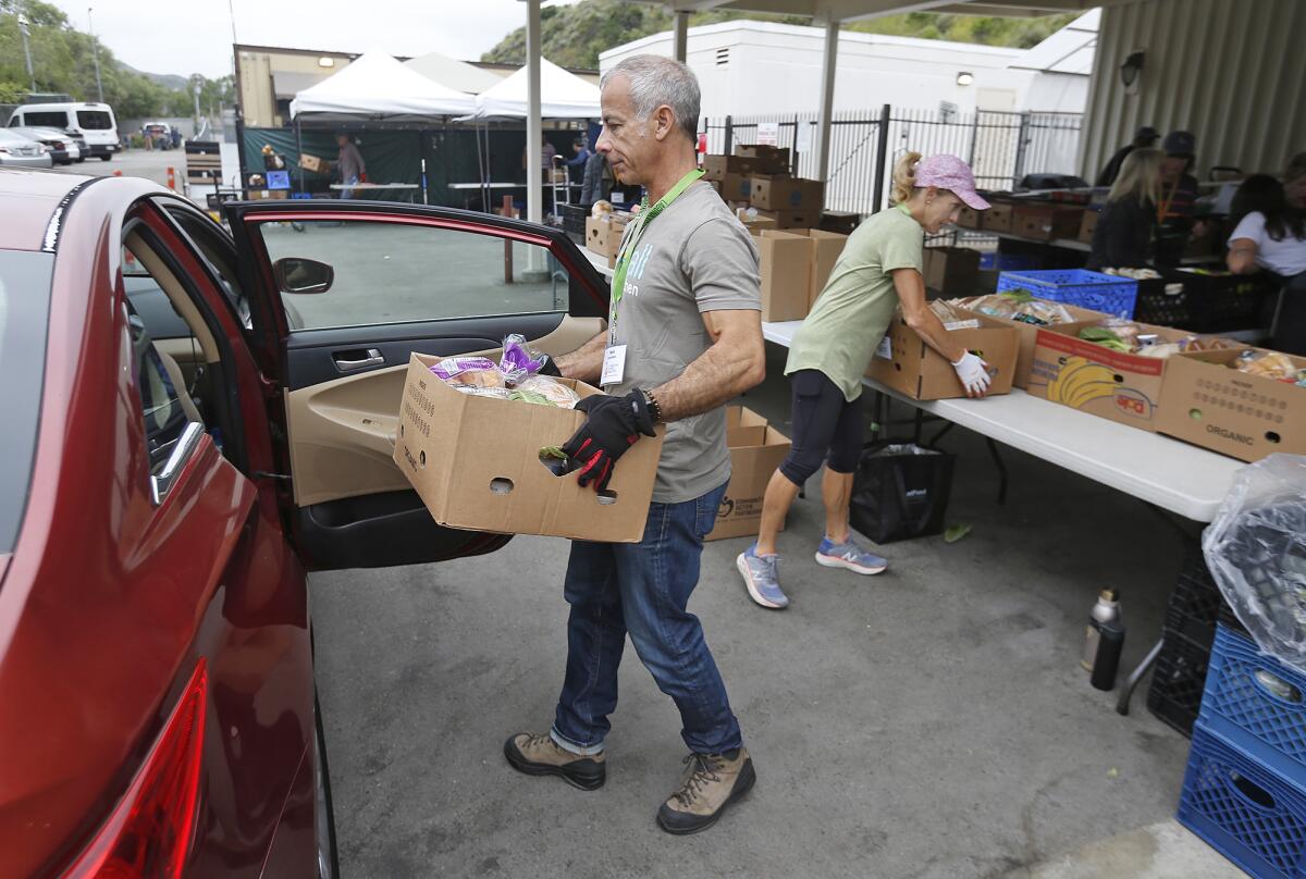 Volunteers Mark James and Mary Ann Sprague, from left, load a car with groceries at the Laguna Food Pantry on Wednesday.