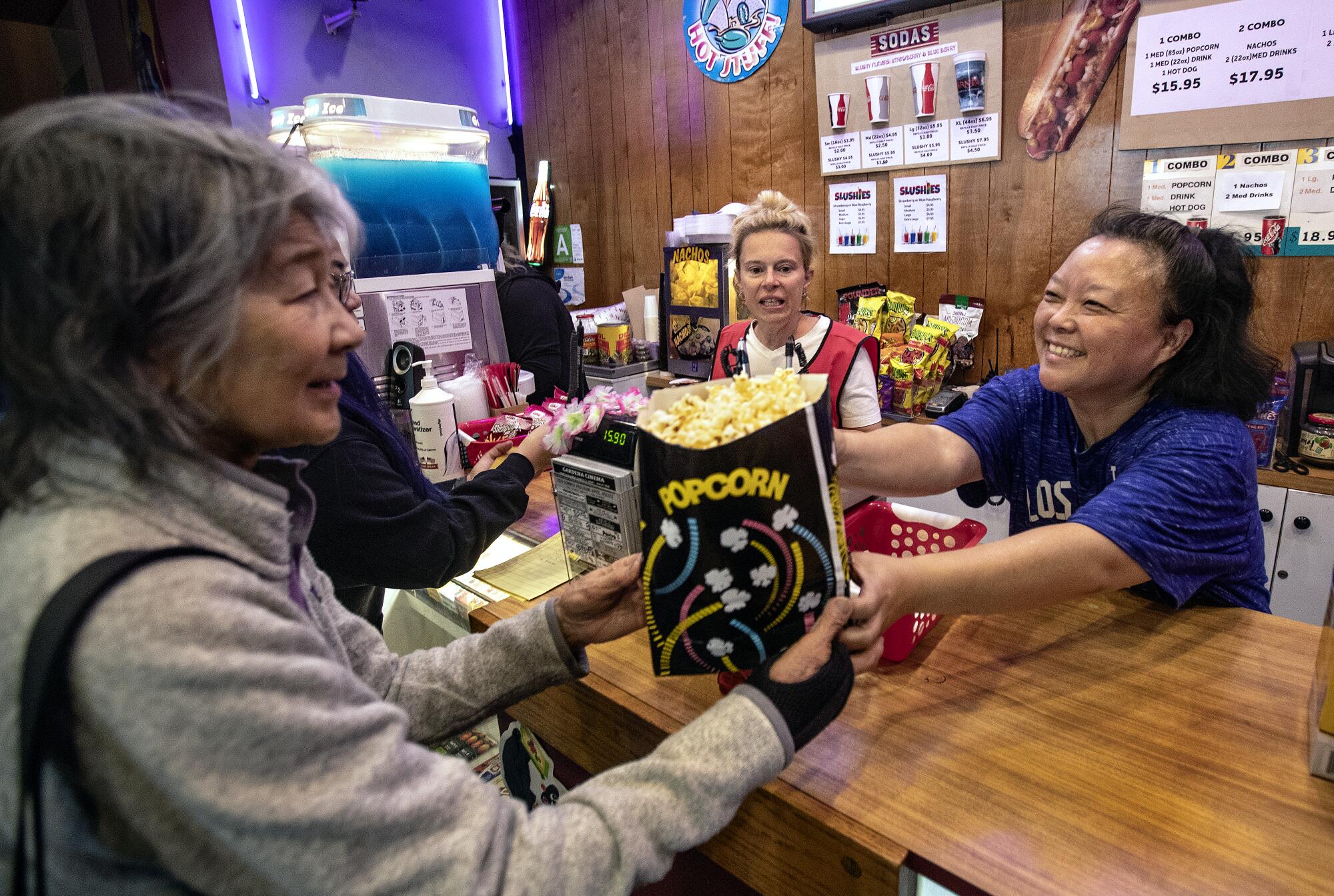 A woman hands a bag of popcorn across a concessions counter to a customer
