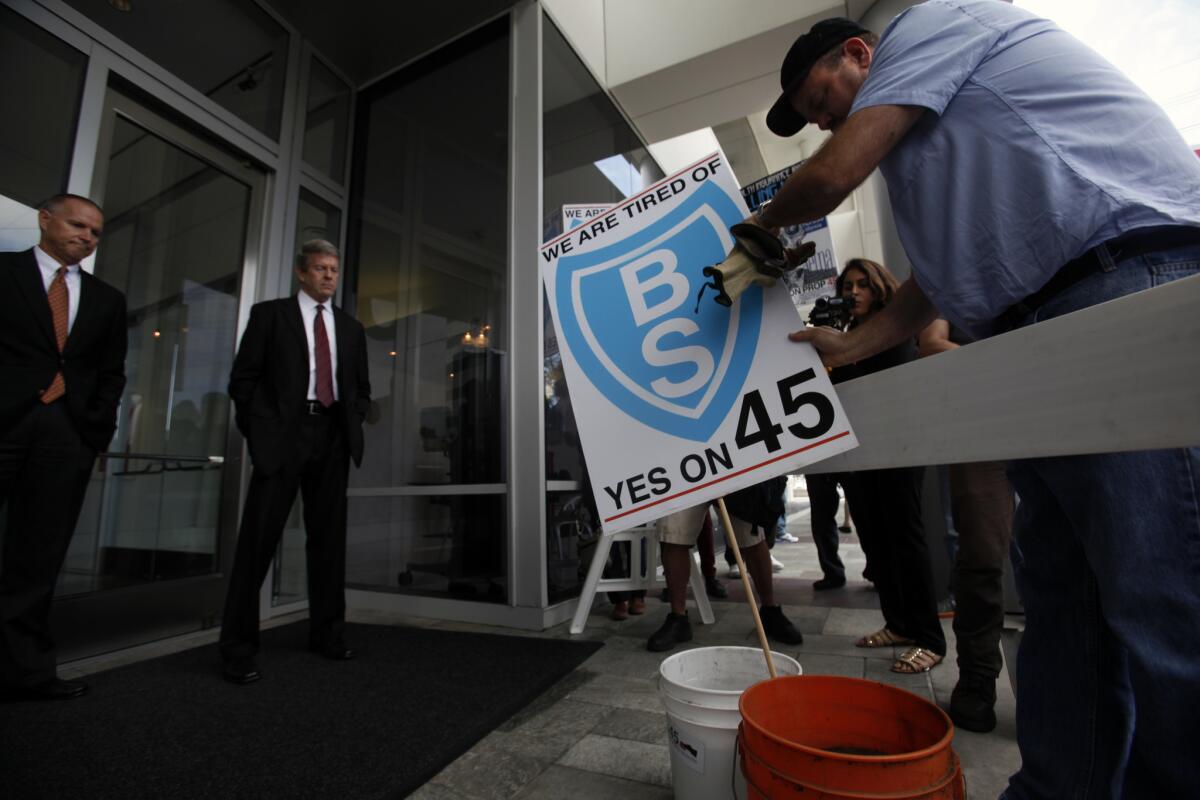 Security guards watch as Jamie Court of the Consumer Watchdog organization places a sign into buckets filled with steer manure outside Blue Shield offices in El Segundo on Oct. 14. The odoriferous message was delivered by Proposition 45 supporters protesting Blue Shield sponsorship of anti-Proposition 45 commercials.