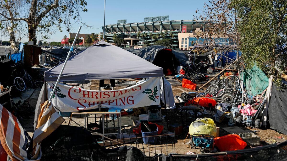 A homeless encampment along the Santa Ana River in Anaheim sits near Angel Stadium in Anaheim, in the background. An advocacy group has filed a lawsuit to stop the county from clearing the encampment.