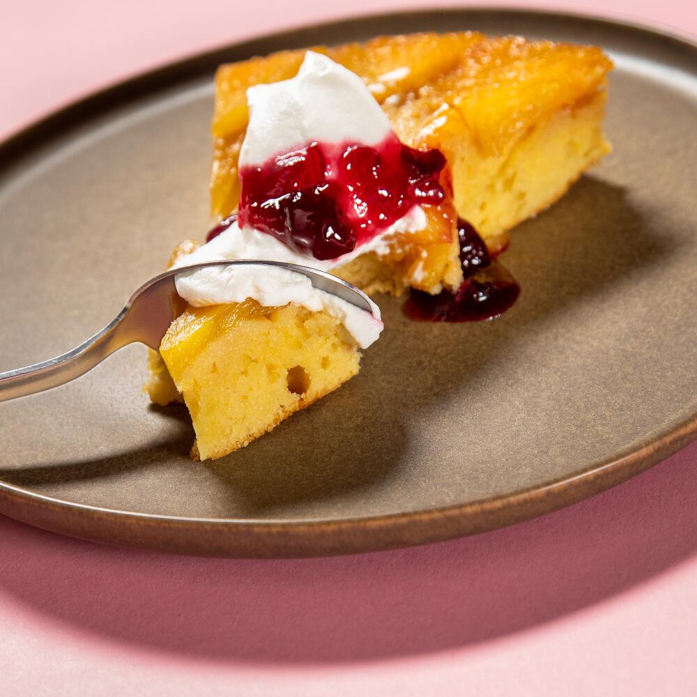 A slice of a pineapple upside-down cake with whipped cream and cherry compote. 
